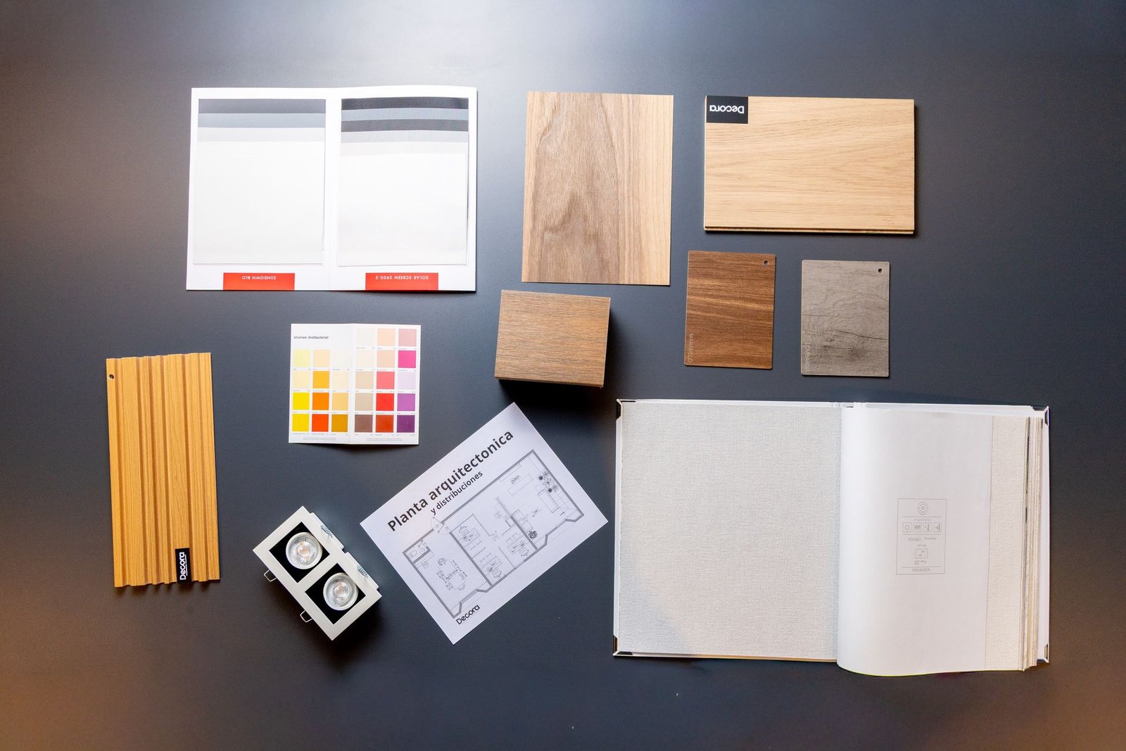 Mesa de trabajo de Decora con muestras de madera, telas, carta de color y planta arquitectónica