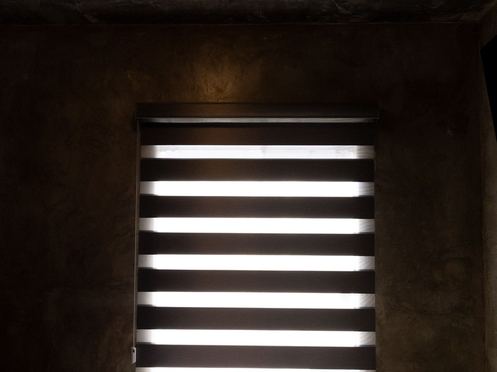 Recámara de estilo industrial con muros de microcemento y persiana zebra, proyecto Decora