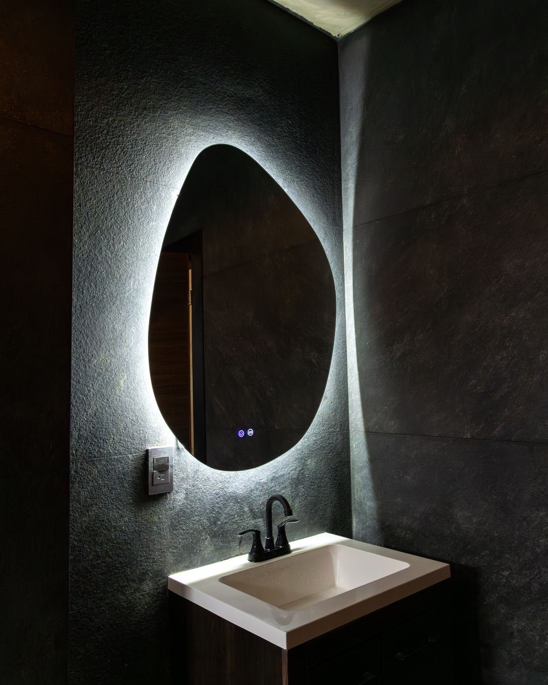 Baño de Hotel Calle 8 con espejo orgánico retroiluminado sobre muro de piedra negra