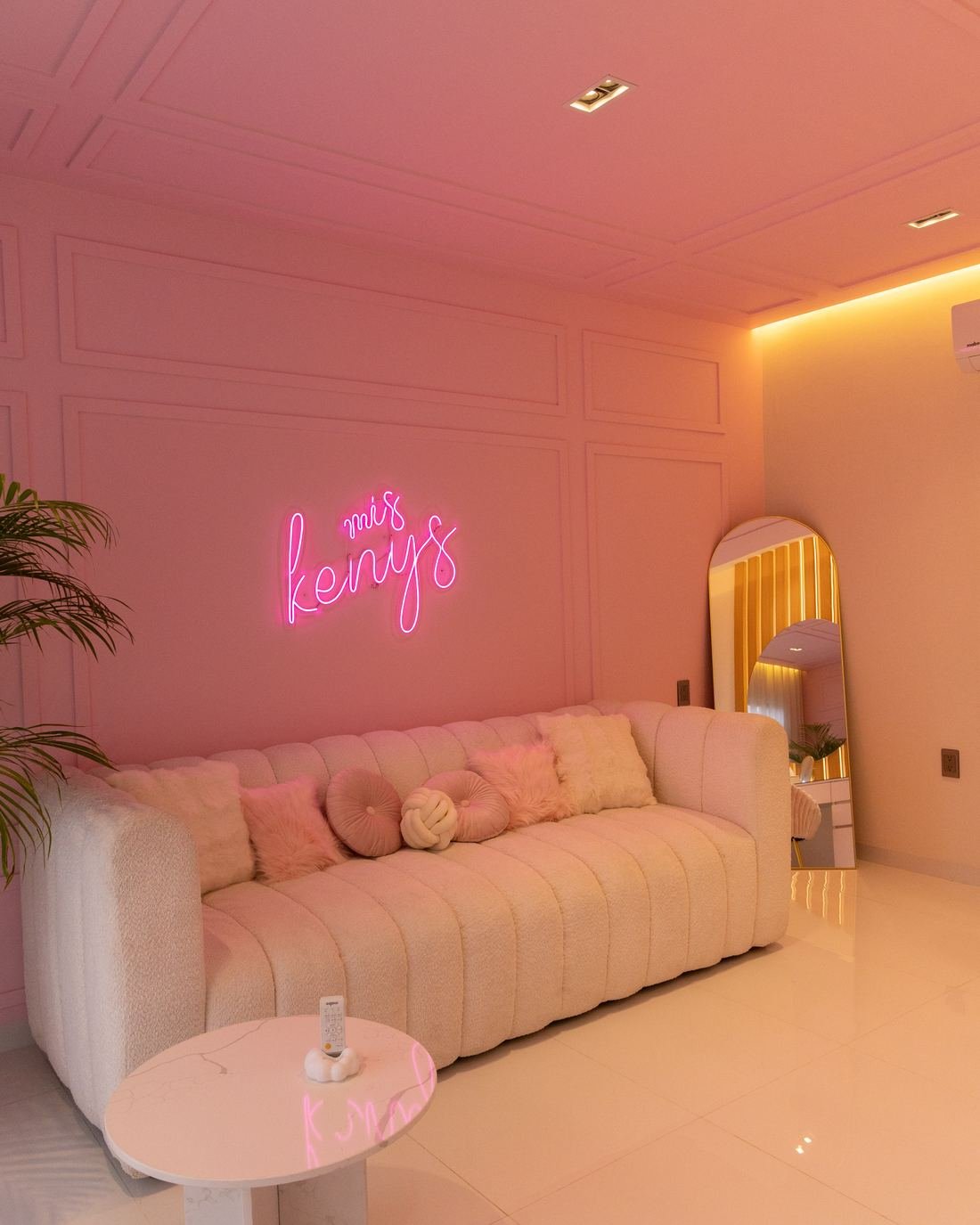 Sala de Estudio Kenedy con muros rosas de molduras, sofá bouclé, letrero de neón y espejo de arco