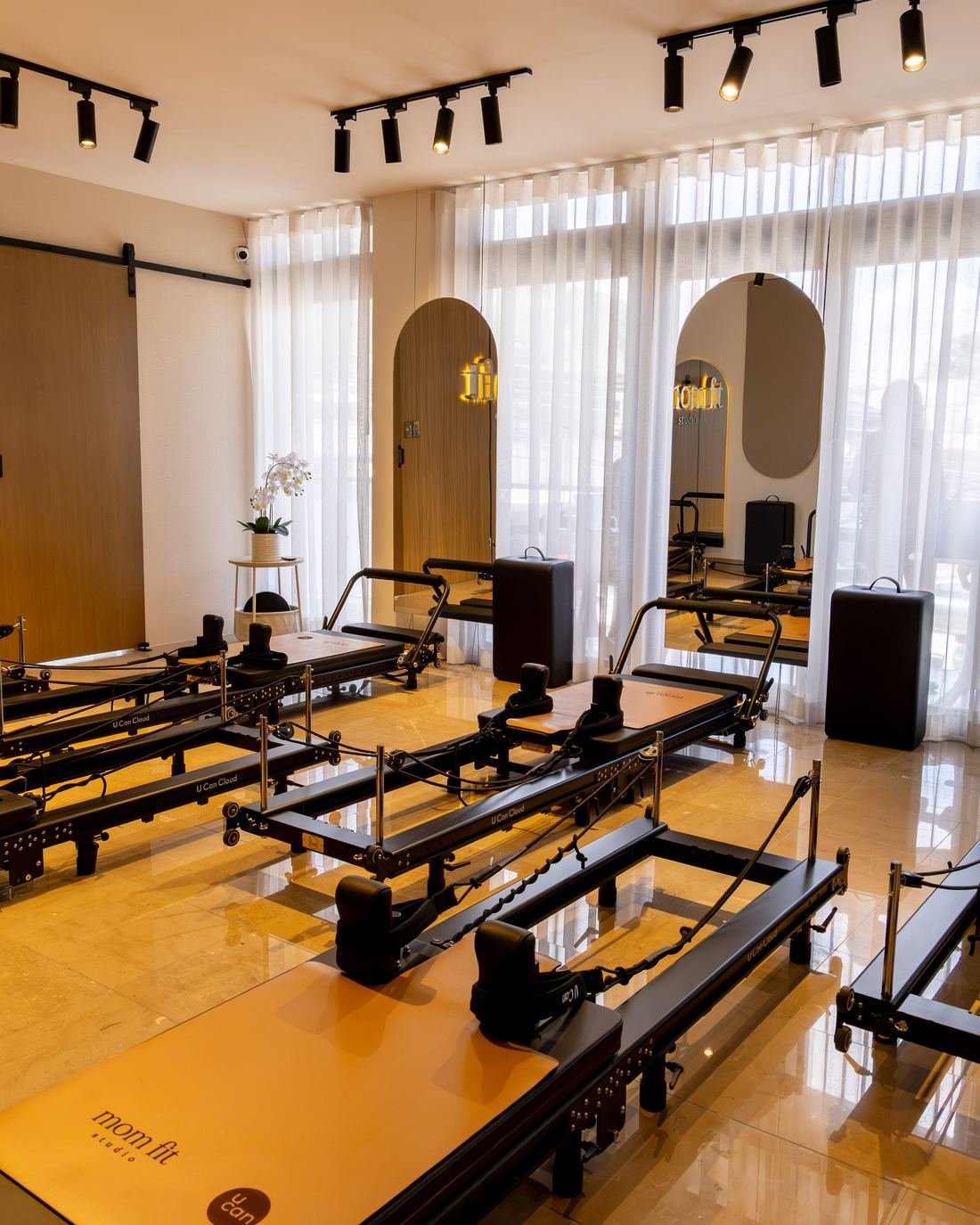 Sala de reformers de Mom Fit Studio con cortinas, espejos de arco y luz cálida